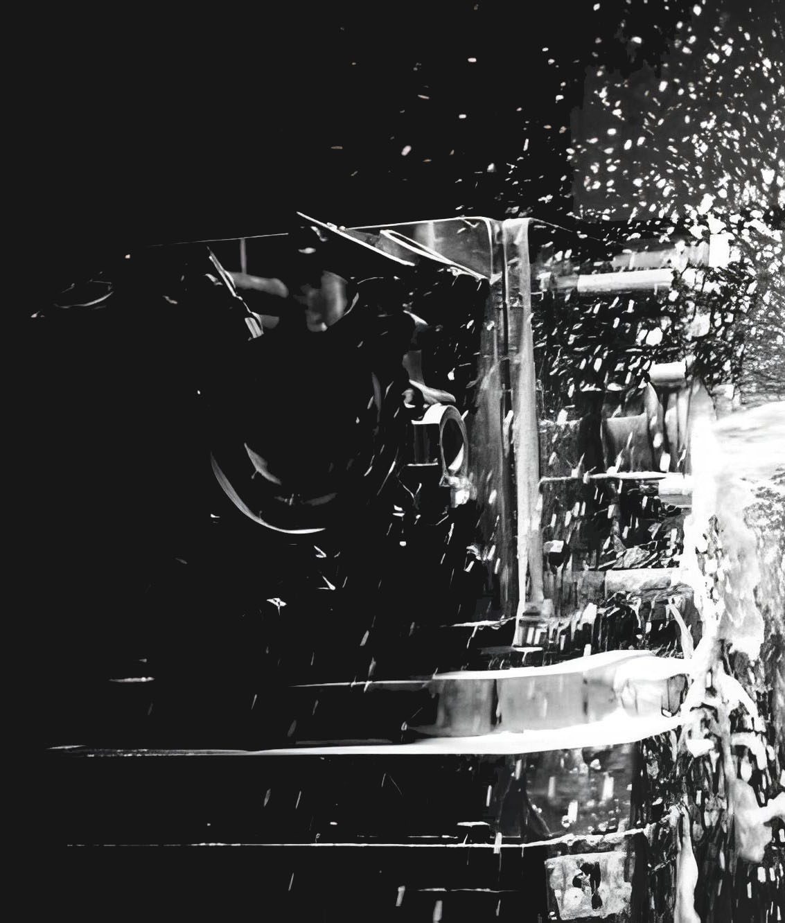Fotografia in bianco e nero di una lavorazione su macchina utensile: l&rsquo;utensile in presa sul pezzo, con truciolo e refrigerante che schizzano